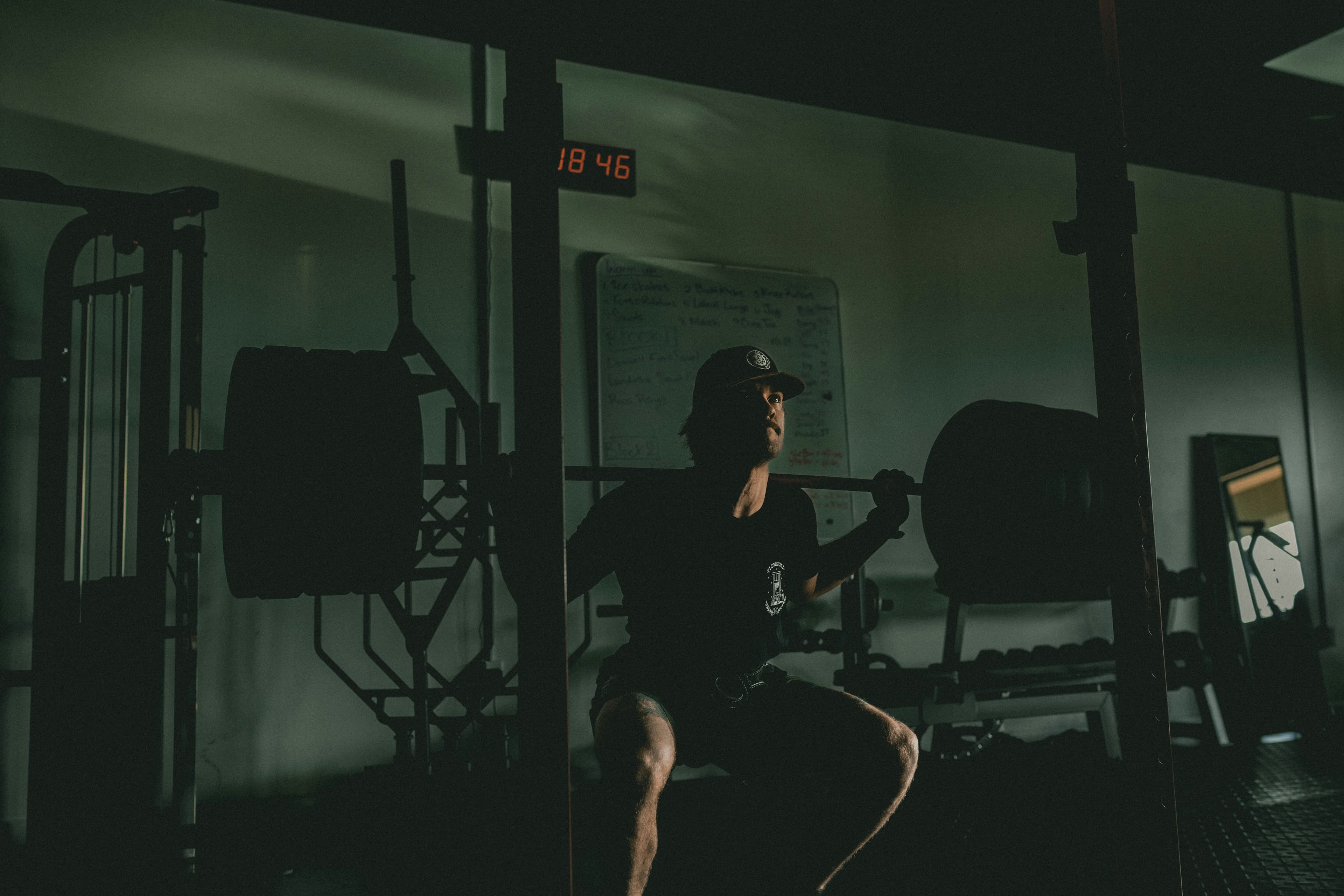 Athlete squatting heavy in a dark gym with a timer glowing overhead